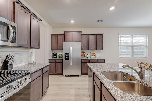 kitchen featuring stainless steel appliances, light stone counters, tasteful backsplash, and sink