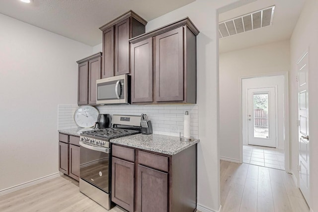 kitchen with backsplash, light hardwood / wood-style floors, dark brown cabinetry, stainless steel appliances, and light stone counters