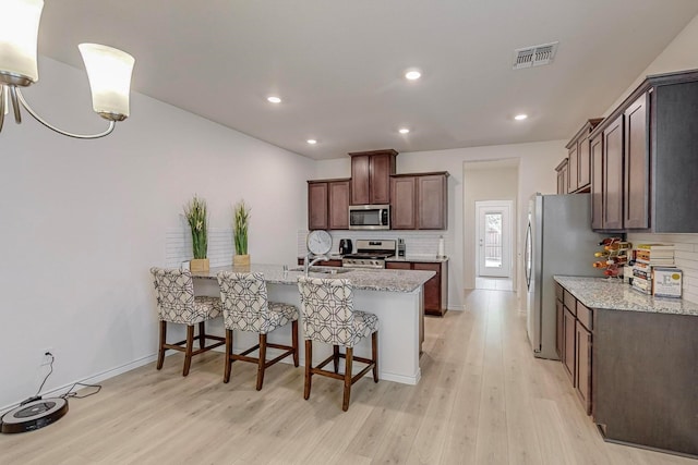 kitchen with light stone countertops, appliances with stainless steel finishes, decorative backsplash, sink, and light hardwood / wood-style floors