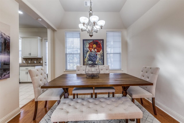 dining room featuring an inviting chandelier, light hardwood / wood-style floors, and vaulted ceiling