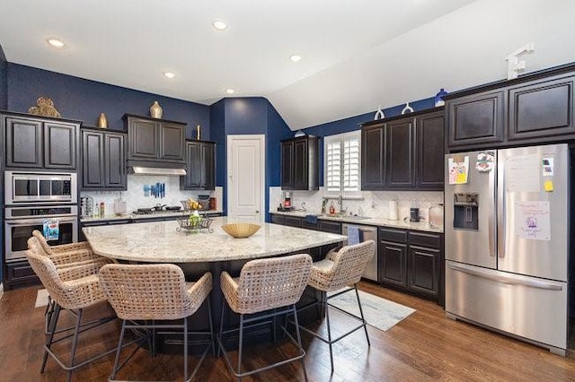 kitchen featuring decorative backsplash, appliances with stainless steel finishes, a kitchen island, and lofted ceiling