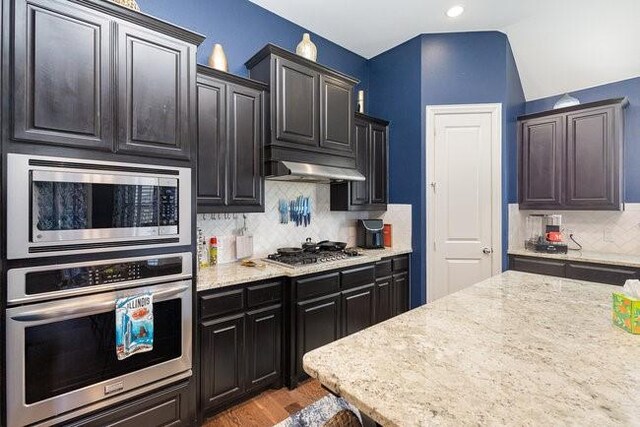 kitchen with light stone countertops, stainless steel appliances, light hardwood / wood-style floors, vaulted ceiling, and decorative backsplash