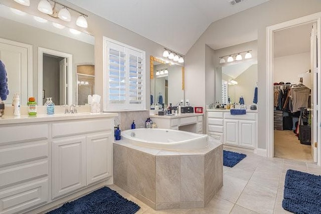 bathroom with lofted ceiling, vanity, a relaxing tiled tub, and tile patterned flooring