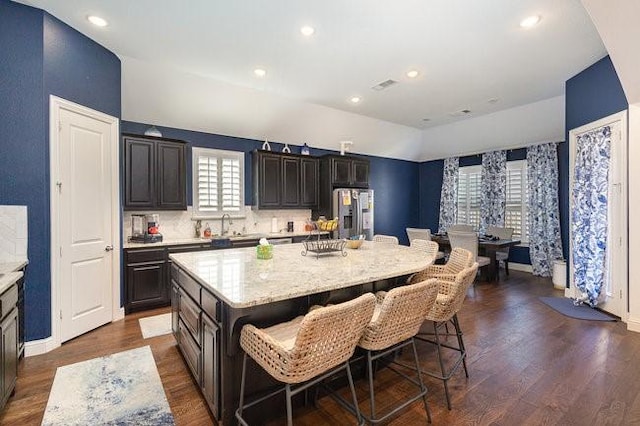 kitchen with dark hardwood / wood-style floors, a kitchen bar, stainless steel fridge, and a kitchen island