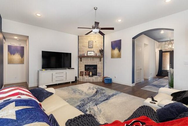 living room with dark hardwood / wood-style flooring, a stone fireplace, and ceiling fan