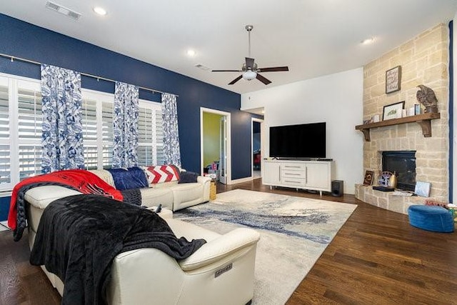 living room featuring a stone fireplace, dark wood-type flooring, and ceiling fan