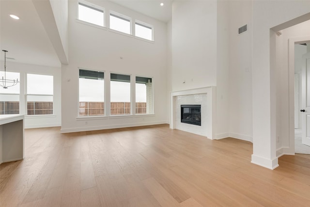 3231 Fisher Rd, Rockwall, TX 75032 - unfurnished living room with a towering ceiling, light wood-style floors, a glass covered fireplace, baseboards, and a chandelier