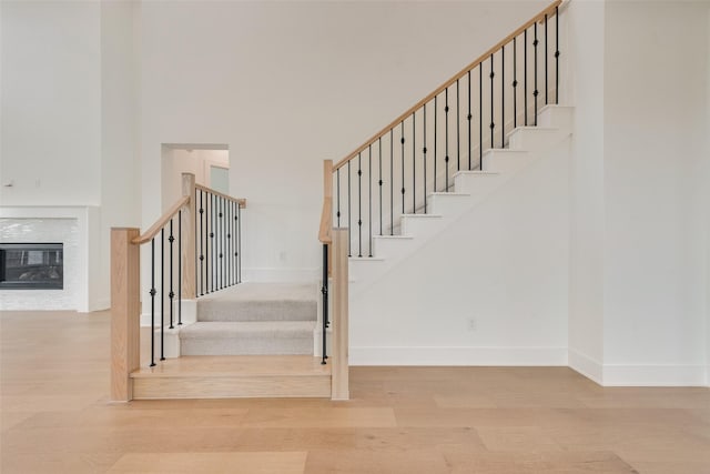 3231 Fisher Rd, Rockwall, TX 75032 - staircase featuring a high ceiling, baseboards, wood finished floors, and a glass covered fireplace