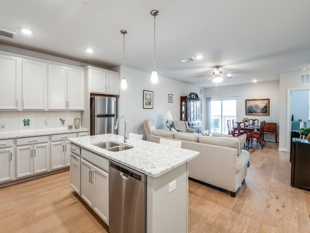 kitchen with white cabinets, hanging light fixtures, an island with sink, appliances with stainless steel finishes, and tasteful backsplash