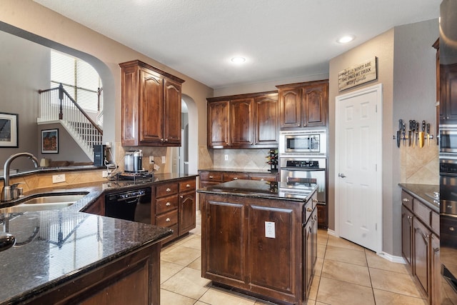 kitchen with sink, light tile patterned floors, dark stone counters, a kitchen island, and appliances with stainless steel finishes