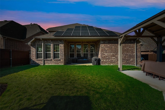 back house at dusk with solar panels, a yard, and a patio