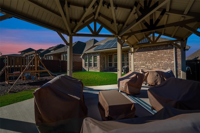 patio terrace at dusk featuring a gazebo, area for grilling, a playground, and a lawn