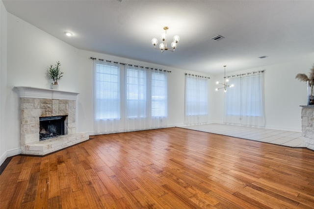 unfurnished living room with an inviting chandelier, light hardwood / wood-style flooring, and a stone fireplace