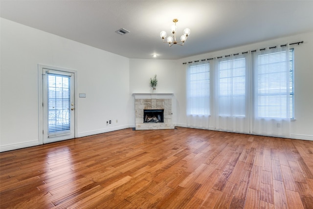 unfurnished living room with wood-type flooring, a fireplace, and an inviting chandelier