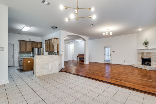 kitchen with light tile patterned floors, kitchen peninsula, backsplash, stainless steel refrigerator, and a chandelier