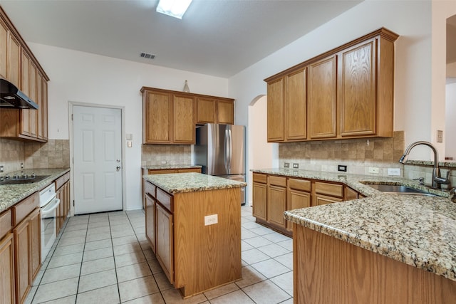 kitchen featuring light stone countertops, sink, stainless steel refrigerator, and a kitchen island