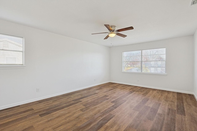 empty room with a healthy amount of sunlight, ceiling fan, and dark wood-type flooring