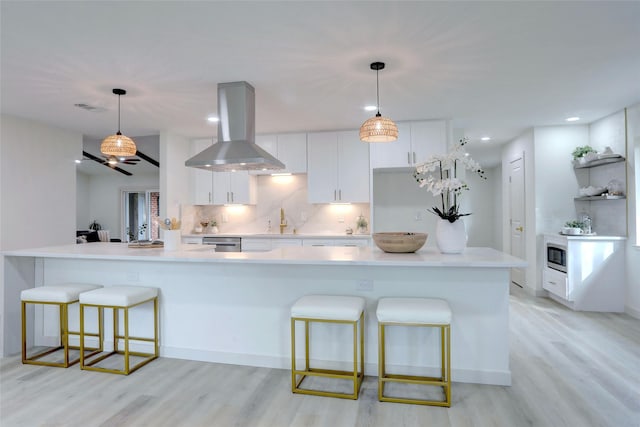 kitchen featuring island exhaust hood, a kitchen bar, white cabinetry, and hanging light fixtures