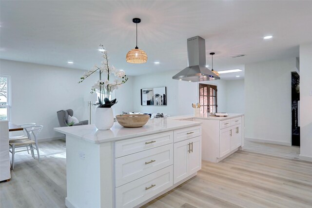 kitchen featuring white cabinetry, light hardwood / wood-style floors, decorative light fixtures, island range hood, and a kitchen island