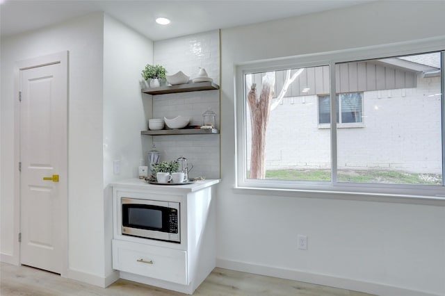 bar with backsplash, white cabinetry, stainless steel microwave, and light hardwood / wood-style floors