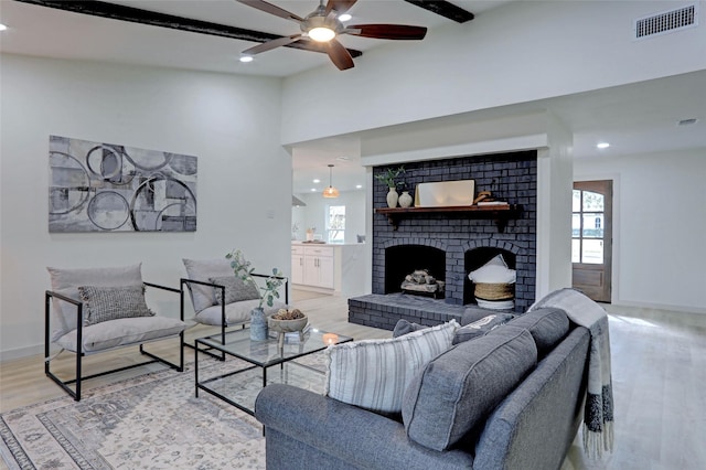 living room with beam ceiling, ceiling fan, light hardwood / wood-style floors, and a brick fireplace