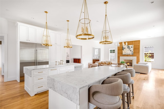 kitchen with light stone countertops, a center island, hanging light fixtures, white cabinets, and light wood-type flooring