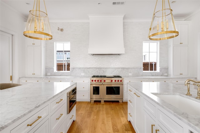 kitchen with double oven range, sink, hanging light fixtures, light wood-type flooring, and white cabinetry