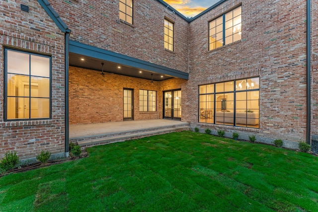 back house at dusk with a patio area and a lawn