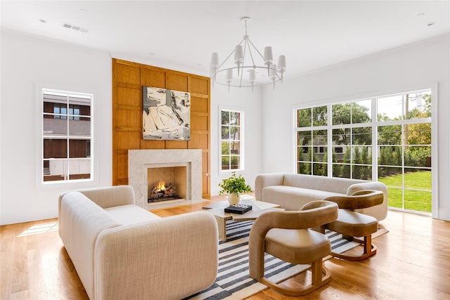 living room featuring crown molding, a high end fireplace, a chandelier, and light wood-type flooring