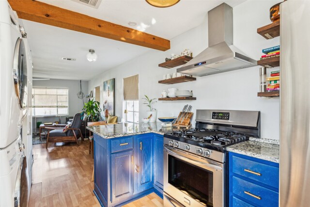 kitchen with blue cabinetry, stacked washer / drying machine, appliances with stainless steel finishes, kitchen peninsula, and island exhaust hood