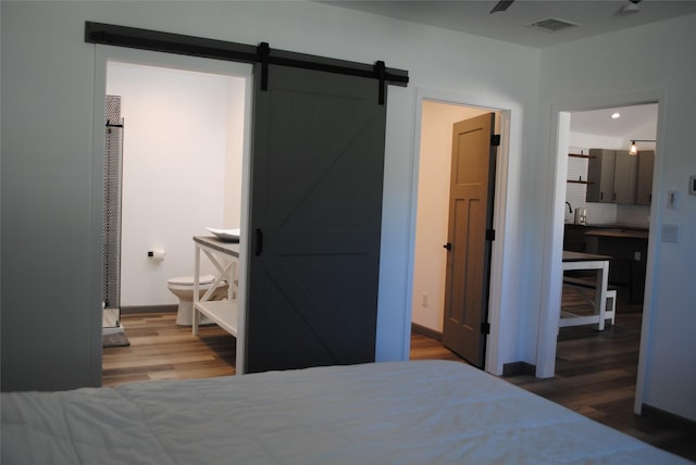 bedroom featuring sink, ensuite bath, dark wood-type flooring, and a barn door