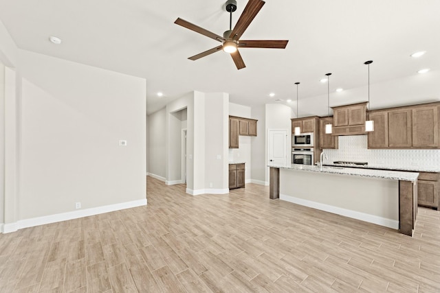 kitchen with oven, built in microwave, light wood-type flooring, decorative backsplash, and brown cabinetry