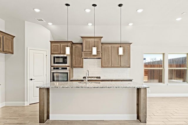 kitchen featuring a kitchen island with sink, oven, built in microwave, backsplash, and light stone countertops