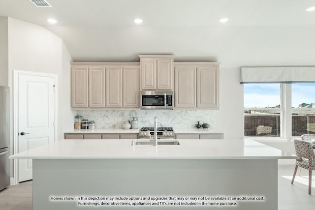 kitchen featuring cream cabinets, a center island with sink, sink, decorative backsplash, and stainless steel appliances