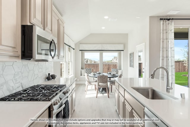 kitchen with sink, stainless steel appliances, vaulted ceiling, decorative backsplash, and light wood-type flooring