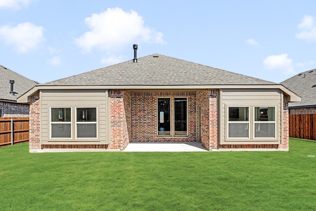 rear view of house featuring roof with shingles, a fenced backyard, a lawn, and brick siding