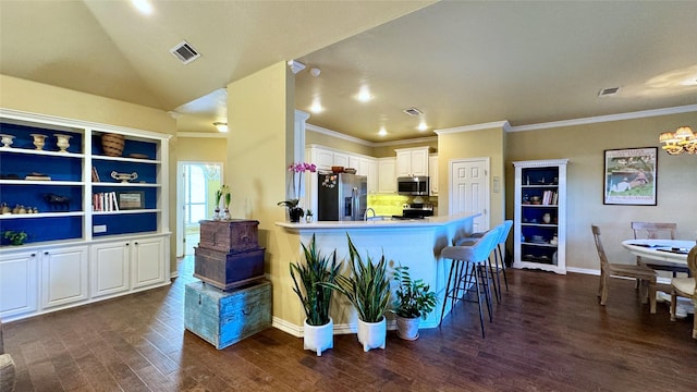 kitchen featuring dark wood-type flooring, white cabinets, appliances with stainless steel finishes, tasteful backsplash, and a breakfast bar area