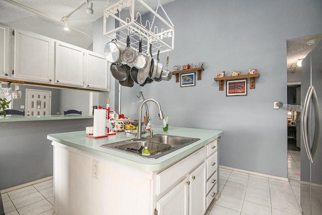 kitchen featuring sink, light tile patterned floors, stainless steel fridge, a kitchen island with sink, and white cabinets