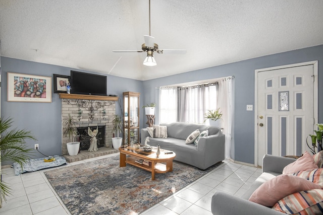 tiled living room with ceiling fan, a textured ceiling, and a brick fireplace