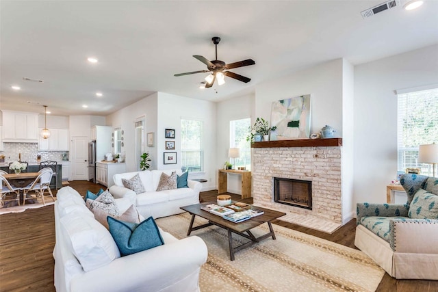 living room featuring a fireplace, ceiling fan, dark hardwood / wood-style flooring, and plenty of natural light