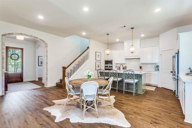 dining area featuring arched walkways, stairway, dark wood finished floors, and recessed lighting