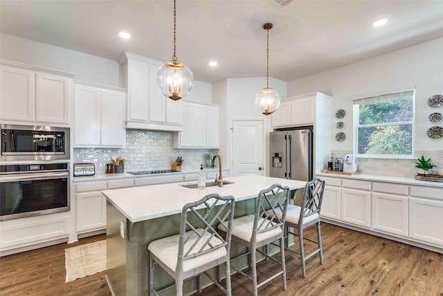 kitchen with white cabinets, appliances with stainless steel finishes, decorative light fixtures, and a kitchen island with sink