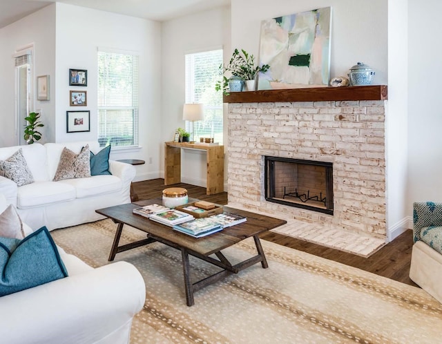 living area with baseboards, wood finished floors, and a stone fireplace