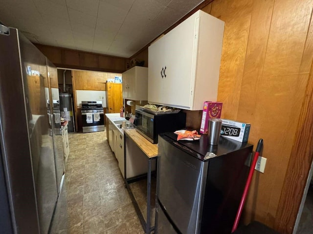 kitchen featuring sink, gas water heater, white cabinetry, appliances with stainless steel finishes, and wooden walls