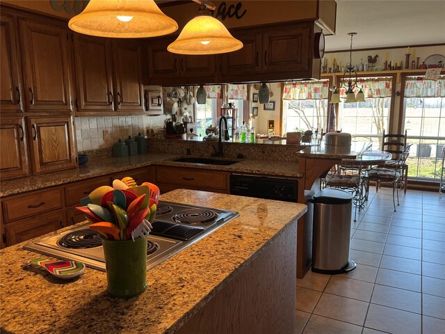 kitchen featuring light stone countertops, stainless steel cooktop, sink, light tile patterned floors, and pendant lighting