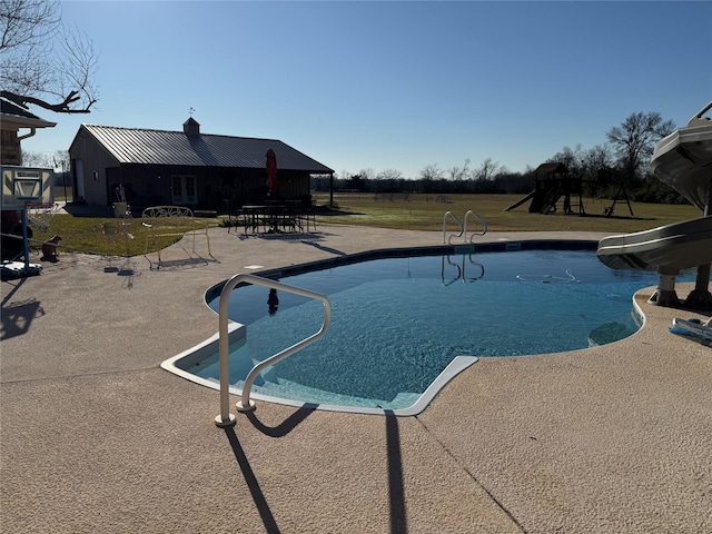 view of swimming pool featuring a yard, a patio, a playground, and a water slide