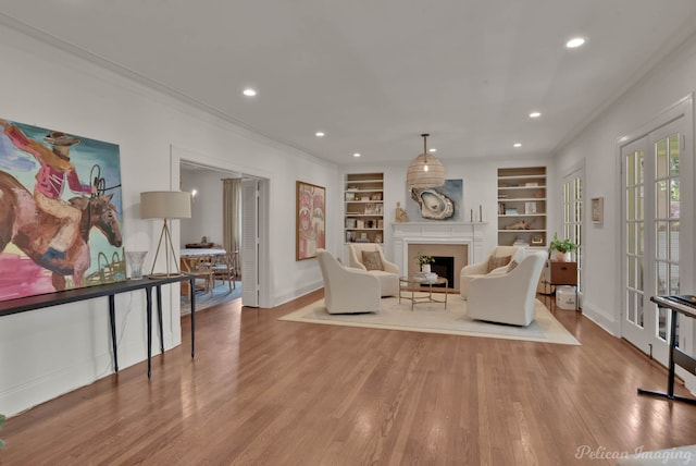 living area with crown molding, built in features, and light hardwood / wood-style floors