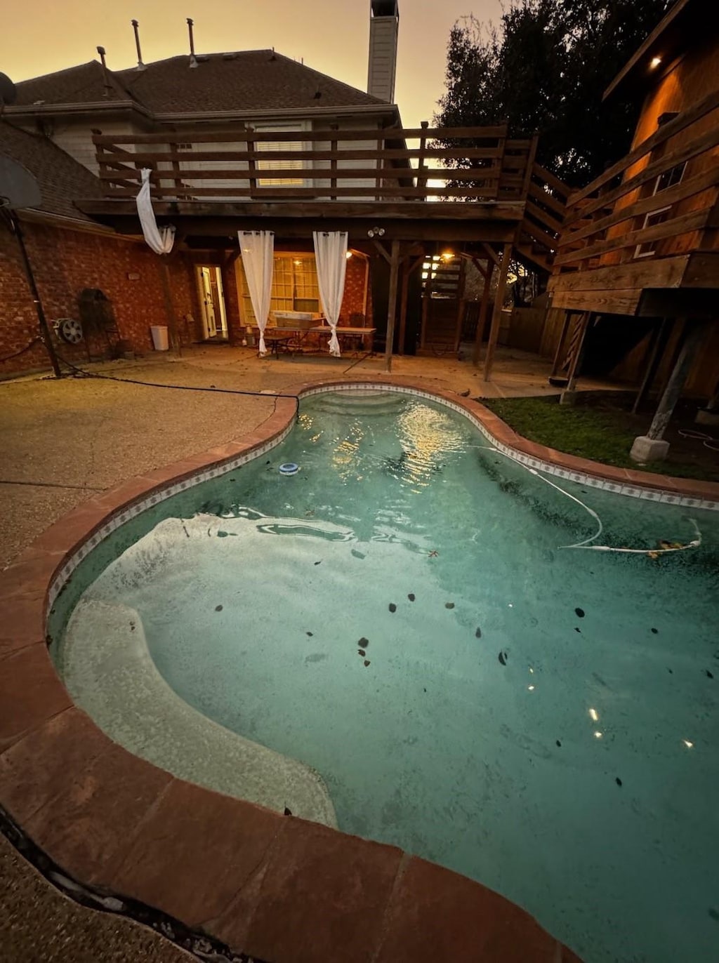 pool at dusk with a patio and a wooden deck