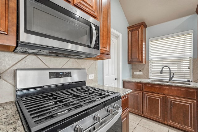 kitchen with stainless steel appliances, sink, light tile patterned floors, and light stone counters