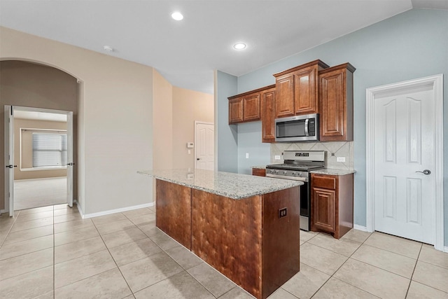 kitchen with light tile patterned flooring, appliances with stainless steel finishes, backsplash, a center island, and light stone counters